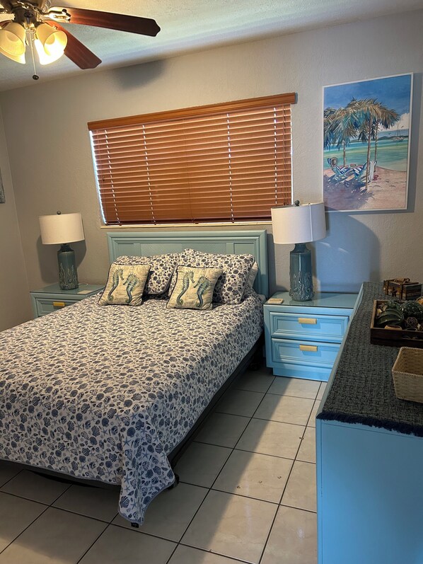A bedroom with a bed, a nightstand, a dresser, a ceiling fan, and a painting on the wall.