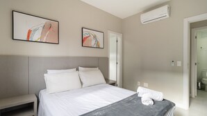Une chambre à coucher moderne avec un lit, une table de chevet, un plaid gris et deux tableaux abstraits accrochés au mur.