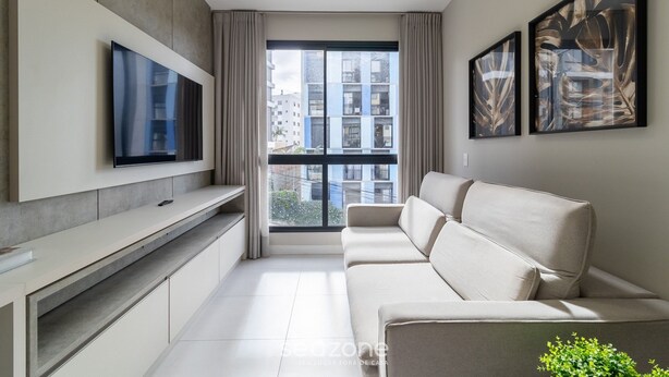 Un salon moderne avec un canapé, un téléviseur à écran plat fixé au mur et deux œuvres d’art encadrées.