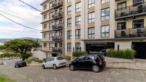 Un immeuble résidentiel à plusieurs étages, doté de balcons, d’une allée pavée et de voitures garées.