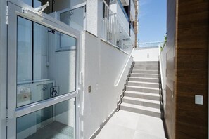 A modern building with a white exterior, a staircase leading to an upper floor, and a glass door with a wheelchair accessibility sign. - SPA - Amazing Studios in Floripa-sc (Florianópolis)