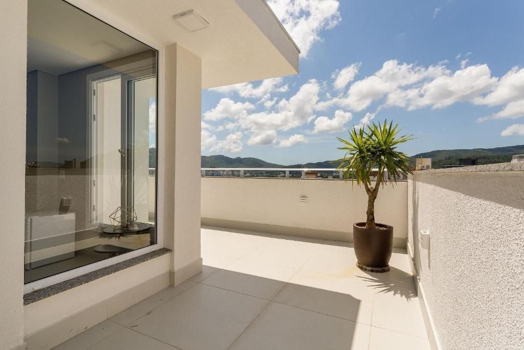 A balcony with a potted plant, a glass door leading to a room, and a clear sky with clouds.