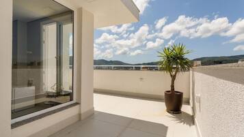 A balcony with a potted plant, a glass door leading to a room, and a clear sky with clouds.