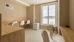 Ett modernt, väl upplyst rum med ett skrivbord i trä, vita stolar, ett litet bord med en geometrisk glasskiva och ett stort fönster med utsikt över havet.