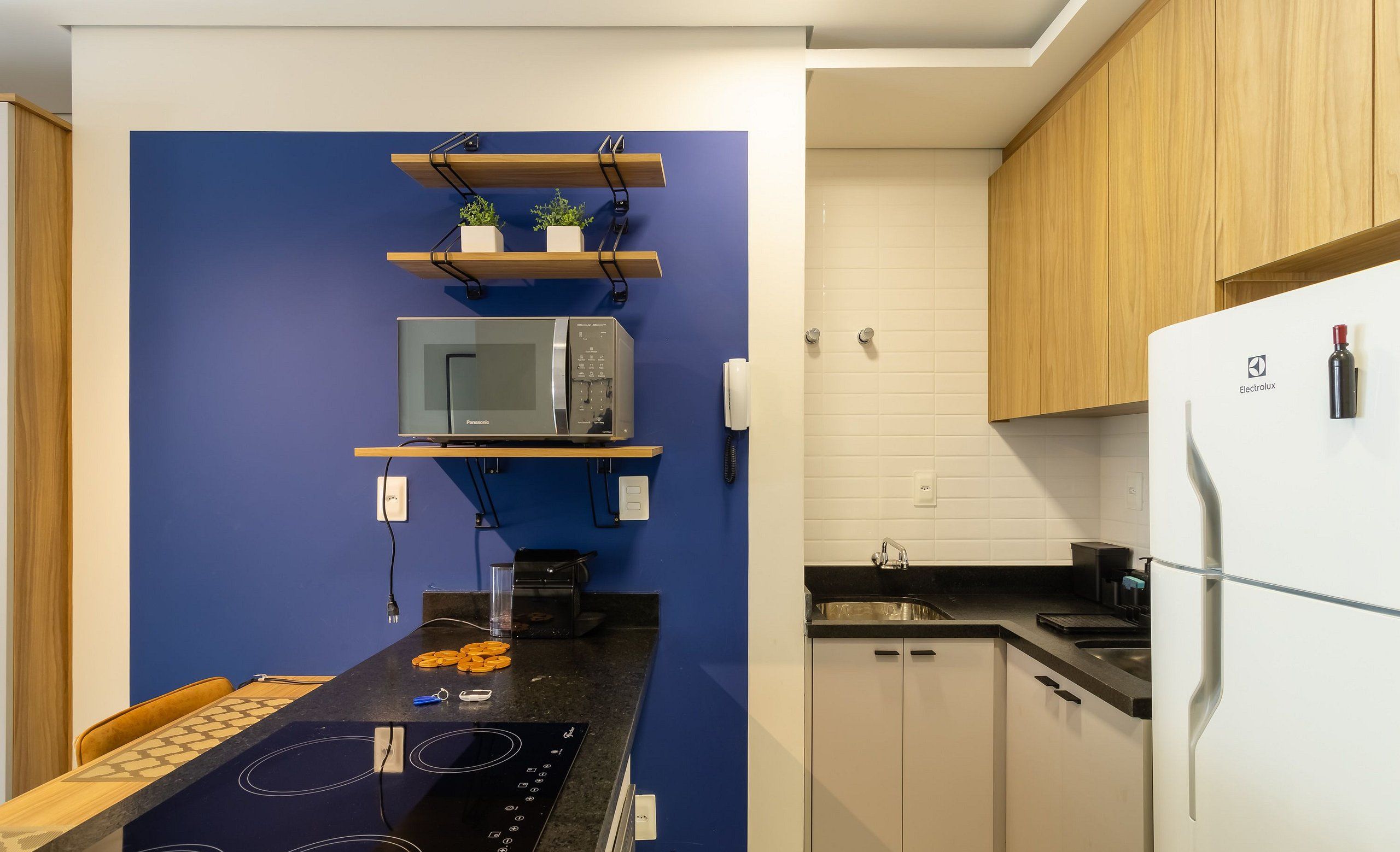 A modern kitchen with a blue accent wall, wooden cabinets, a white refrigerator, and a built-in microwave.