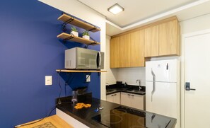 A modern kitchen with a black countertop, a built-in microwave, a stove, and wooden cabinets. - SPA - Amazing Studios in Floripa-sc (Florianópolis)