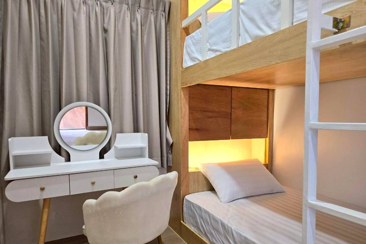Uma cama beliche com cabeceira de madeira, uma escrivaninha branca com um espelho e uma cadeira.