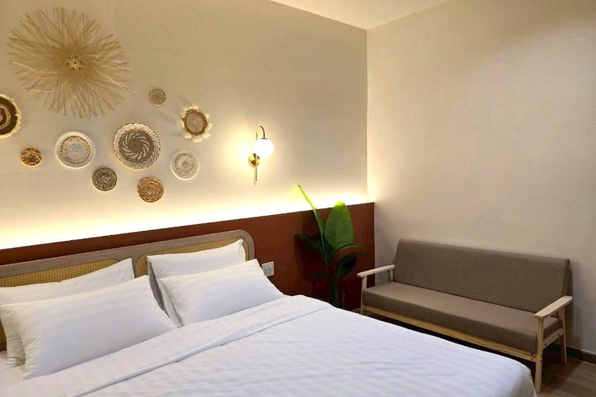 Quarto de hotel com cama, sofá, arte decorativa na parede e luminária fixada na parede.