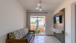 A room with a sofa, a ceiling fan, a TV mounted on the wall, and a balcony with a table and chairs.