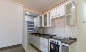 Une cuisine de taille réduite avec des meubles blancs, une cuisinière à gaz et un four encastré.