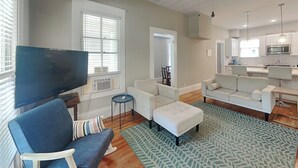 Un salon moderne avec un téléviseur à écran plat, un canapé bleu, un fauteuil blanc et un tapis à motifs.