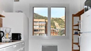 A kitchen with a window view of a building with balconies, a coffee maker, and a built-in oven.
