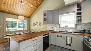 A kitchen with a wooden ceiling, grey cabinets, a wooden countertop, and a window with a view of trees. - Streamside | Nature-Lux w/ Hot Tub, Sauna, Firepit, Game Area, Beautiful Setting (Traverse City)