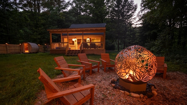 A wooden deck with outdoor seating and a decorative spherical light fixture. - Streamside | Nature-Lux w/ Hot Tub, Sauna, Firepit, Game Area, Beautiful Setting (Traverse City)