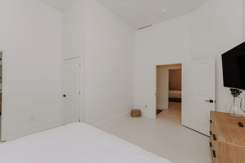 Ein schlicht eingerichtetes Schlafzimmer mit einem großen Bett, einer Holzkommode und einem Fernseher an der Wand.