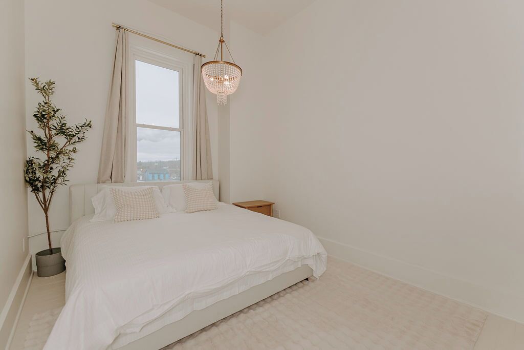 Un dormitorio minimalista con una cama grande, una mesita de noche, una planta en maceta y una ventana con cortinas.