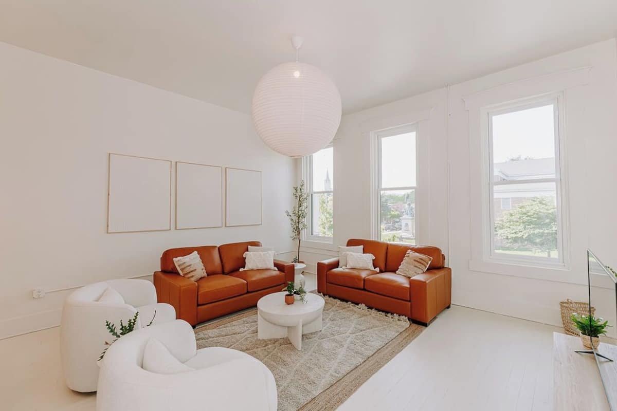 Una sala de estar moderna con dos sofás de cuero marrón, una mesa de centro blanca y una lámpara colgante grande de color blanco.