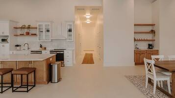 A modern kitchen with white cabinetry, a central island, and bar stools. There is a dining area with a wooden table and chairs.