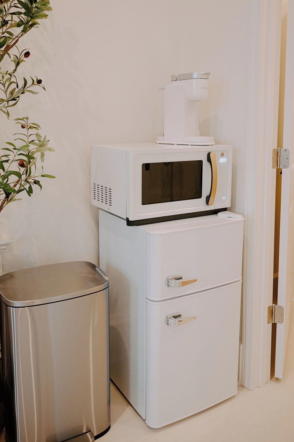 Uma cozinha compacta equipada com micro-ondas e um refrigerador pequeno, uma lixeira e uma porta para um quarto.