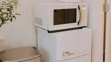 Uma cozinha compacta equipada com micro-ondas e um refrigerador pequeno, uma lixeira e uma porta para um quarto.