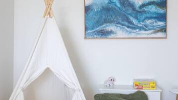 A room with a white teepee, a green bean bag, a framed abstract painting, and a small white table with a toy and a box.