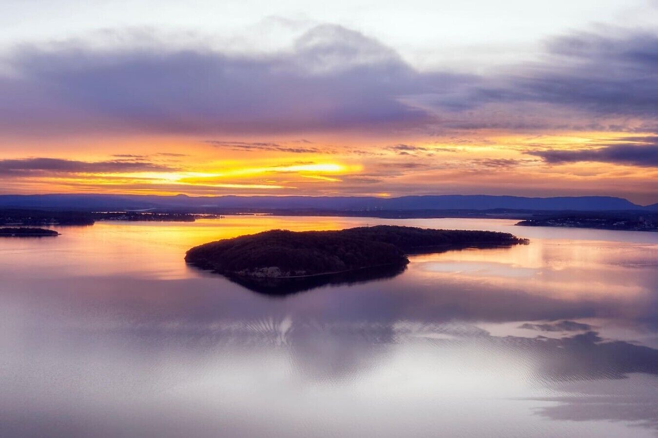 A tranquil sunset over a calm lake with an island in the center.