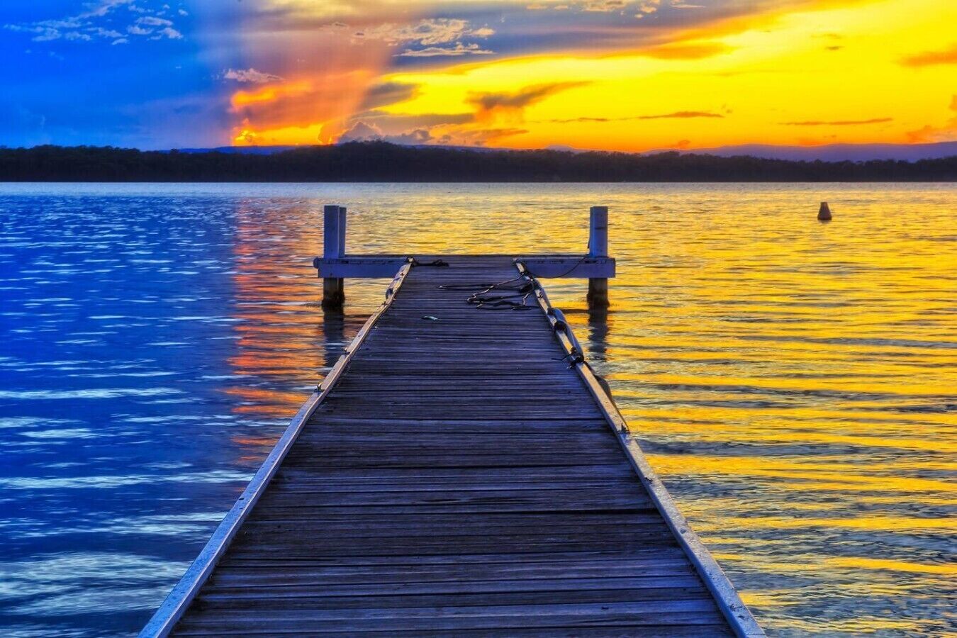 Un muelle de madera se adentra en aguas tranquilas con un atardecer al fondo.