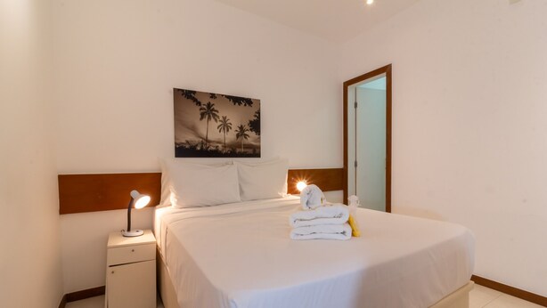 Habitación de hotel con cama, mesita de noche con lámpara, un cuadro de palmeras y un espejo.