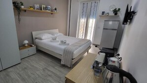 A bedroom with a bed, bedside table, wardrobe, and a small kitchenette area. - B&B Nonno Walter (Torre del Greco)