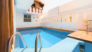 Una piscina con muelle de madera y una estructura con techo de paja al fondo.