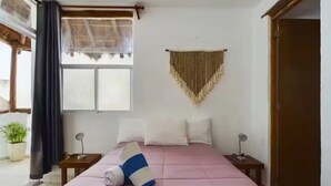 Un dormitorio con una cama grande, dos mesitas de noche, una ventana con cortinas, un adorno en la pared y una puerta.