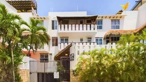 Un edificio moderno con entrada protegida, varios balcones y exuberante vegetación tropical.