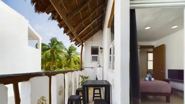 Un balcón con barandilla de madera, una mesa pequeña con dos sillas y vistas a palmeras.