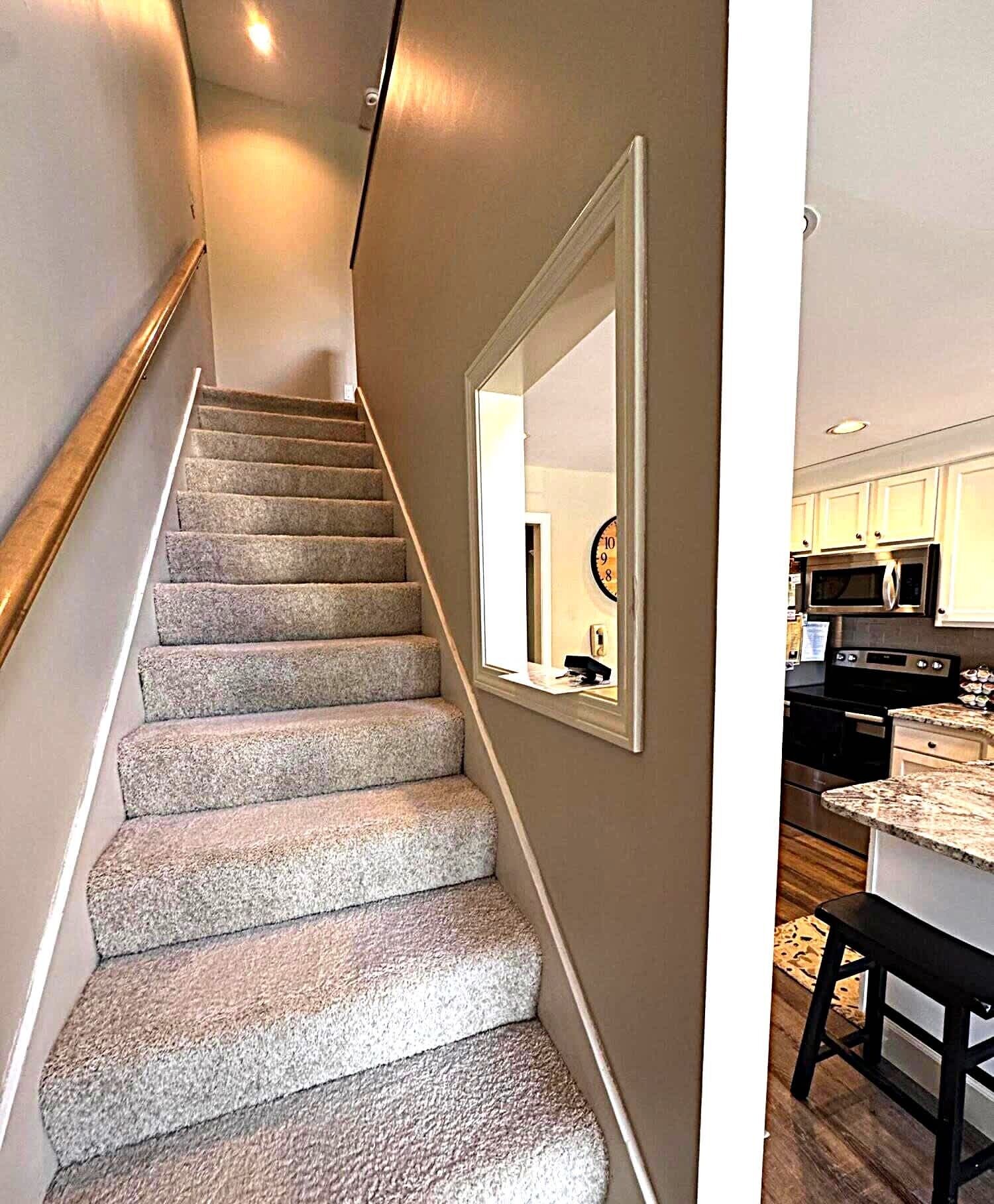 Una escalera con peldaños alfombrados que conduce a una zona de cocina con microondas y armarios.