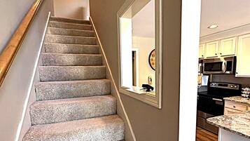 Una escalera con peldaños alfombrados que conduce a una zona de cocina con microondas y armarios.