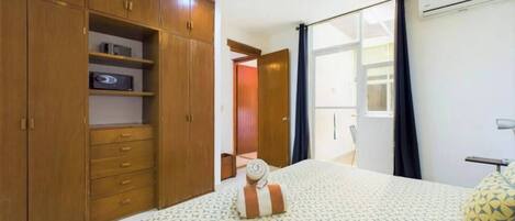 Ein Schlafzimmer mit Bett, Kleiderschrank, Schreibtisch und einem fenster mit Vorhängen.