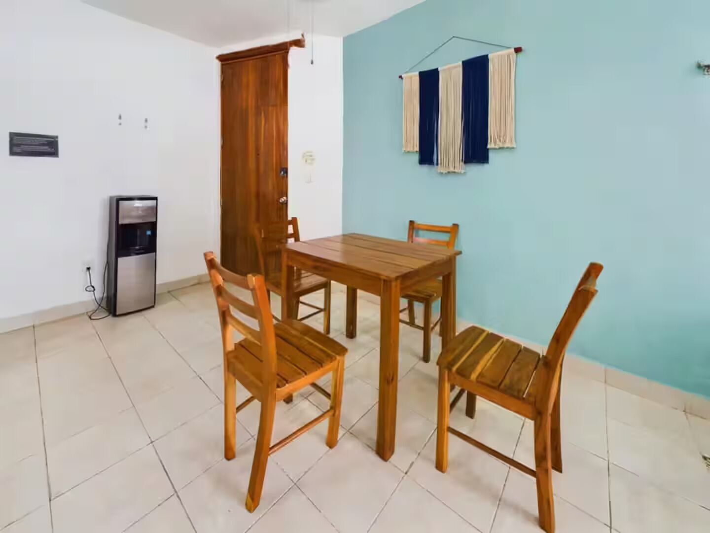 Uma área de refeições com mesa e cadeiras de madeira, um refrigerador e uma parede azul com roupa pendurada.