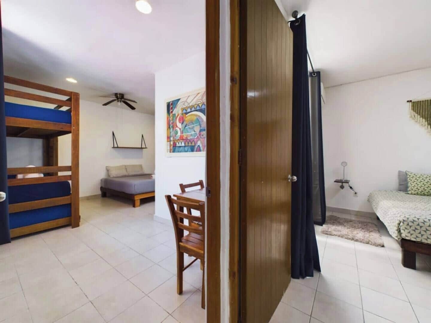 Une chambre avec des lits superposés, un lit simple, une chaise, un ventilateur de plafond et un tableau accroché au mur.