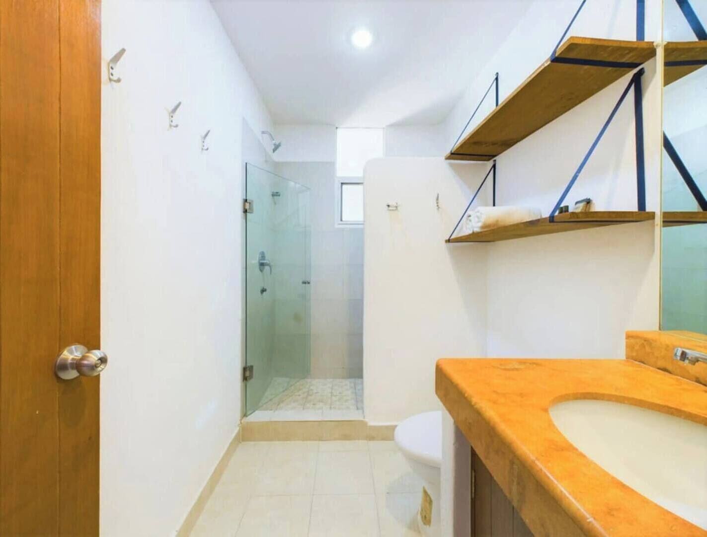 Ein Badezimmer mit Holztür, Duschkabine aus Glas, weißem WC und Holzwaschbecken mit Spiegel.