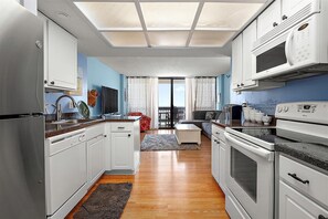 Una cocina moderna con armarios blancos, horno empotrado, microondas y un comedor con mesa y sillas.