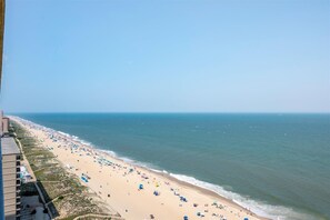 Una playa con una extensa franja de arena, algunos sombrillas y un edificio a la izquierda.