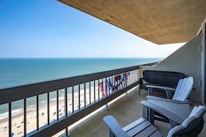 Varanda com vista para a praia e oceano, com mesa e cadeiras.