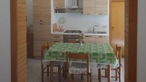 Un coin repas avec une table recouverte d’une nappe verte, des chaises en bois et un luminaire suspendu au-dessus.
