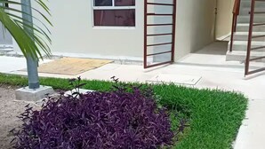 A building with a concrete staircase, a metal gate, and a small garden with purple and green plants. - Aldea Tulum 1st floor (Aldea Tulum)