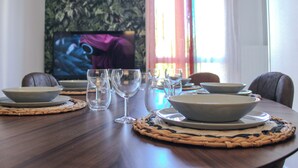 Een eettafel gedekt met kommen en glazen, een televisie op de achtergrond en een raam met gordijnen.