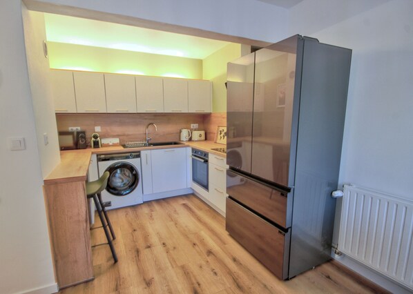 A compact kitchen with a washing machine, a refrigerator, and wooden flooring. - Rennes - 5 rooms, 2 bathrooms - Ideal for groups & professionals (Rennes)