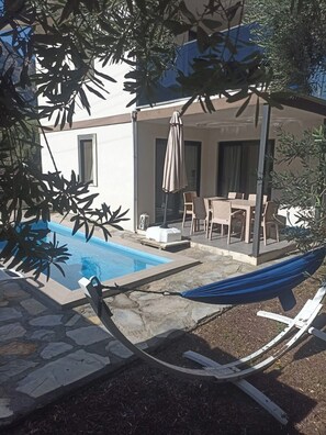 A pool area with a hammock, lounge chairs, and a covered patio with a table and chairs.
