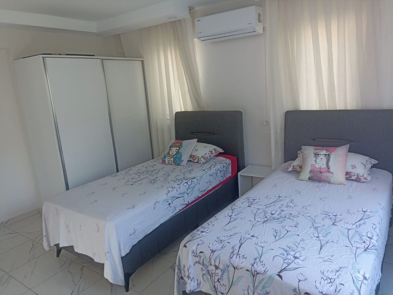 A bedroom with two single beds, a wardrobe, and an air conditioning unit.