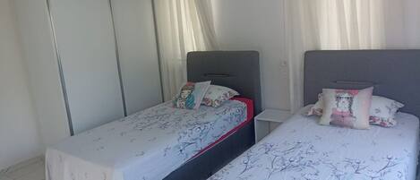 A bedroom with two single beds, a wardrobe, and an air conditioning unit.