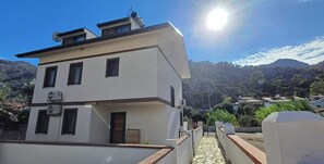 Un bâtiment moderne à deux étages, doté d’un toit plat, d’un petit balcon et d’un chemin pavé menant à l’entrée.